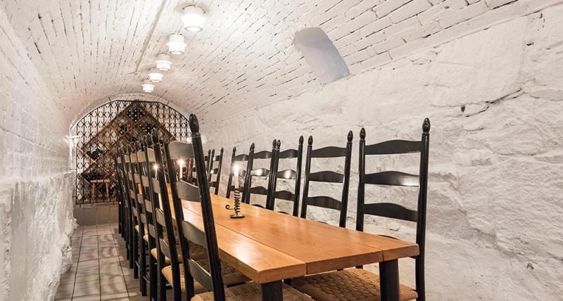Ett långsmalt mötesbord med höga stolar i ett murat gammalt källarvalv som är vitmålat.