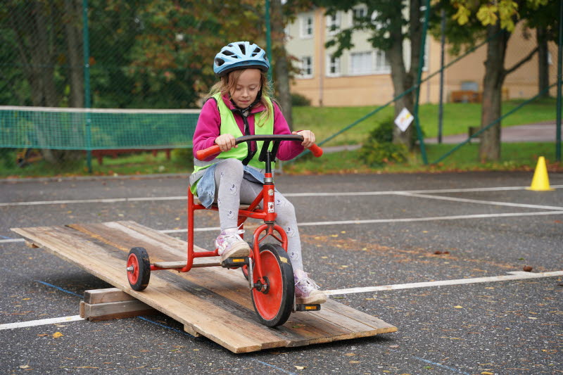 Flicka på trehjuling cyklar över en vippbräda