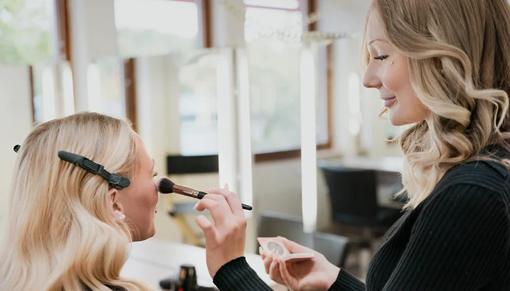 En elev lägger makeup på en modell i salongsmiljö.