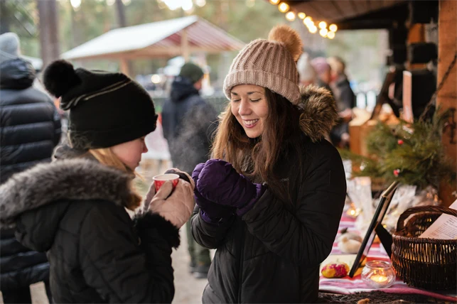 Två tjejer i vinterkläder dricker något varmt ur muggar utomhus