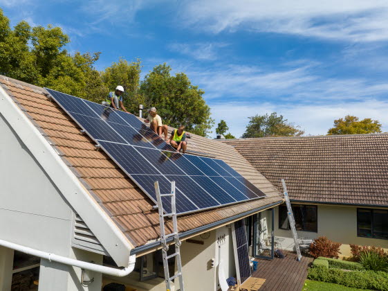 Tre personer monterar solcellspaneler på ett hustak.