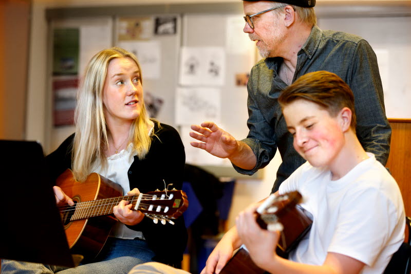 Två elever och en lärare som spelar gitarr i ett klassrum