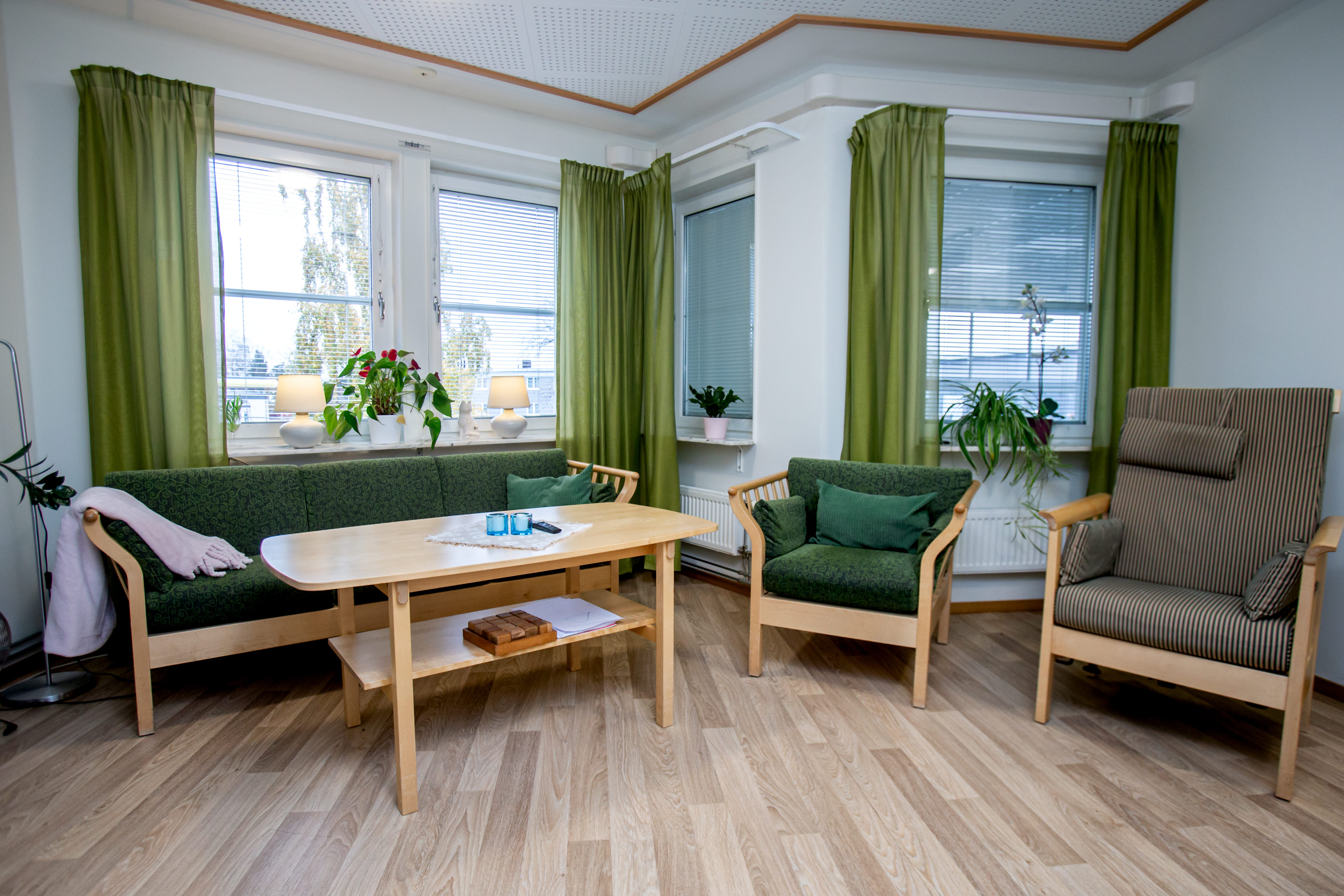 Gemensam social yta med två fåtöljer en soffa och ett bord. Möblerna är klädda i gröna och bruna toner