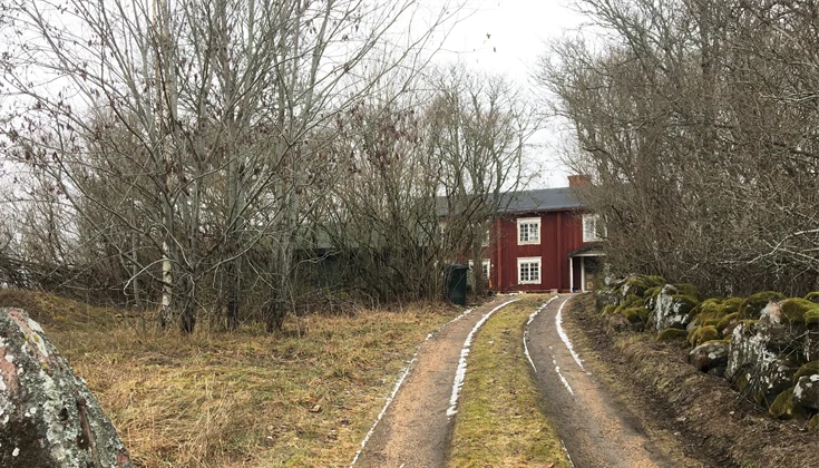 En grusväg som leder fram till ett rött trähus