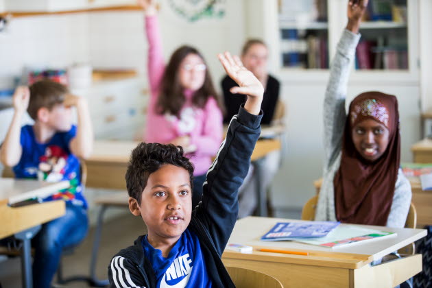 Elever i ett klassrum räcker upp handen.
