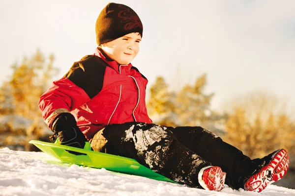 Ett barn sitter i en pulka i en backe