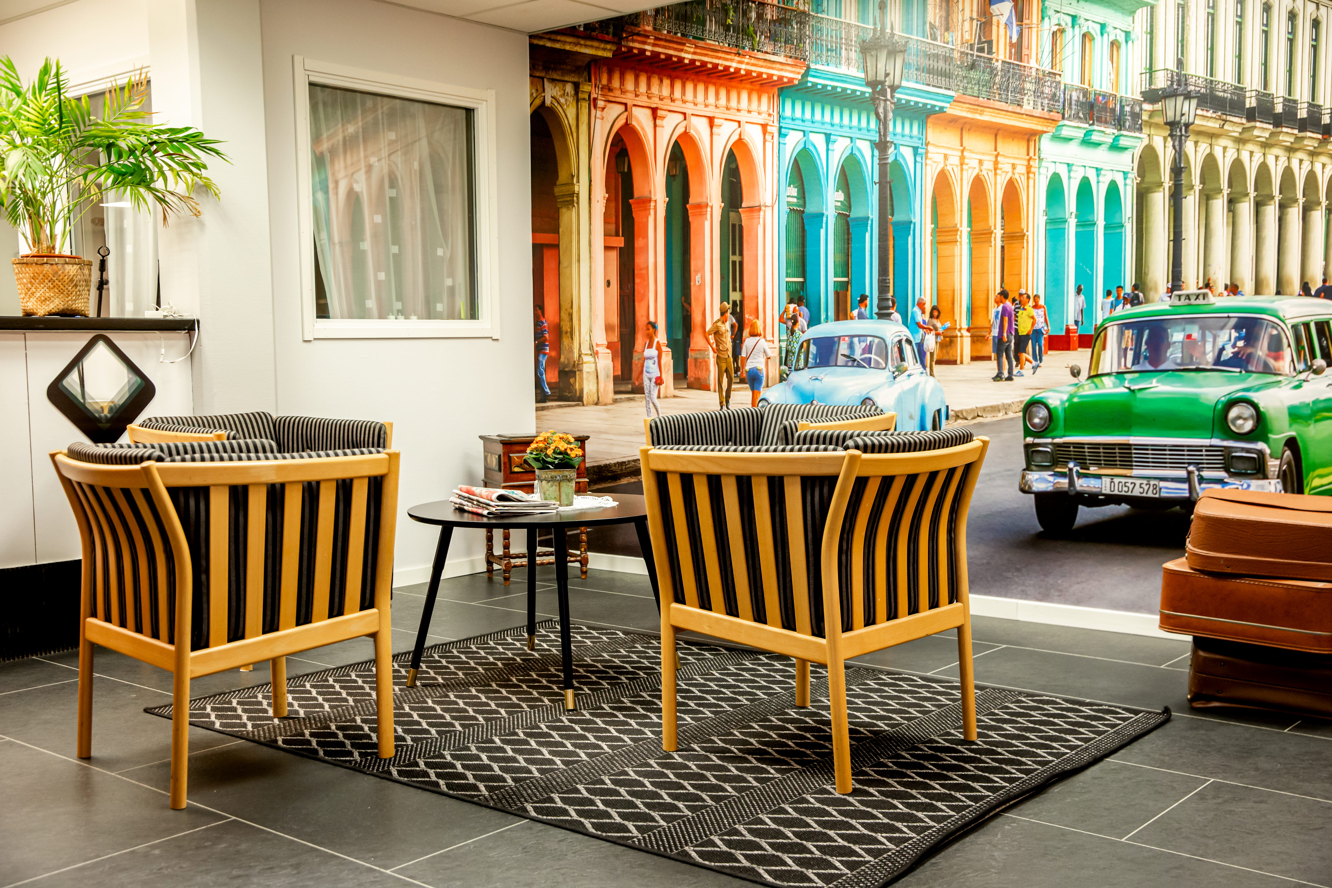 Fåtöljer, matta och ett bord med en färgglad fototapet i bakgrunden som föreställer gamla bilar i stadsmiljö