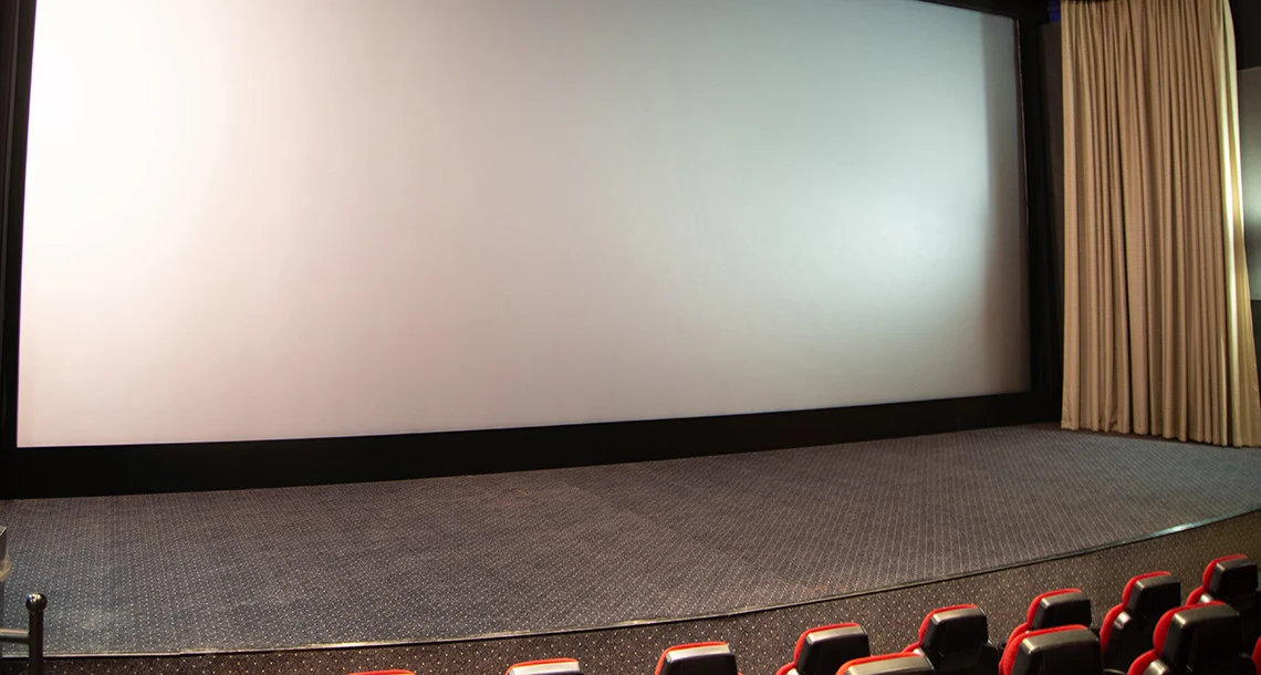 En stor filmduk framför en tom scen där första raden med stolar syns