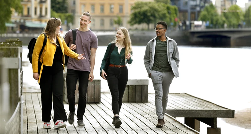 Fyra personer som pratar och går på en brygga vid vattnet.