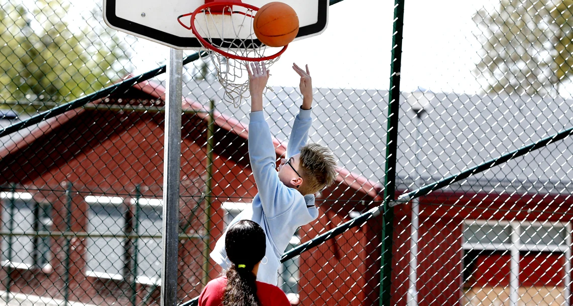 två ungdomar spelar basket på skolgården