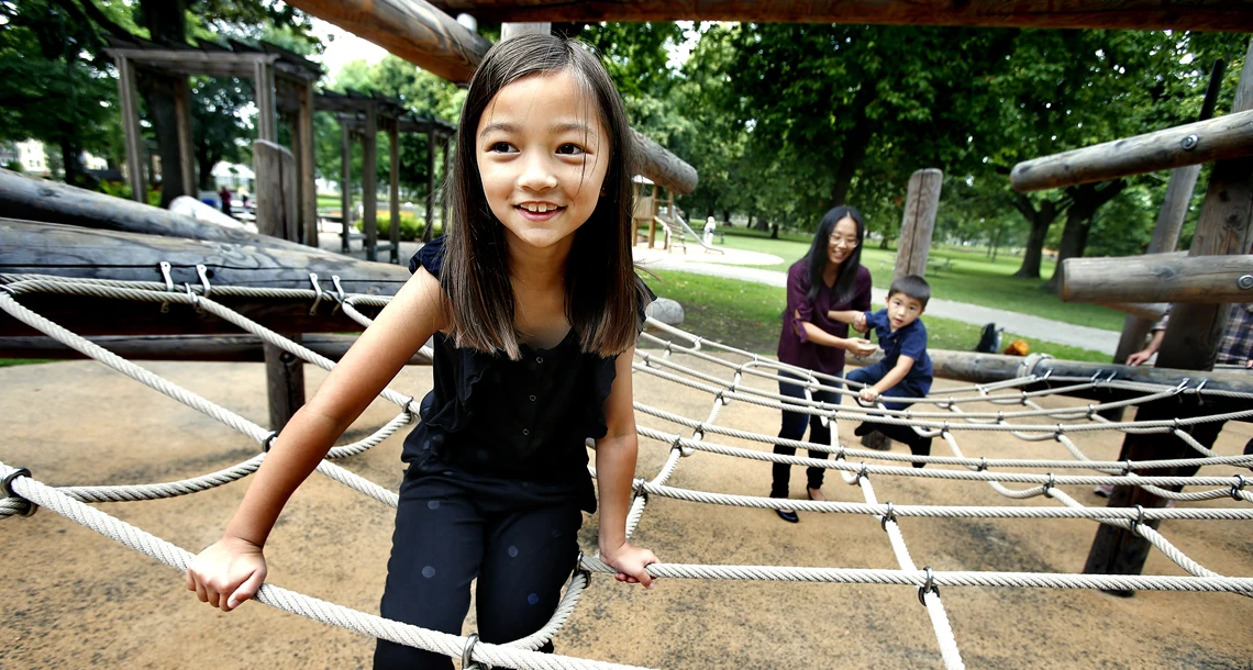 Flicka klättrar i ett nät och en kvinna och pojke syns i bakgrunden