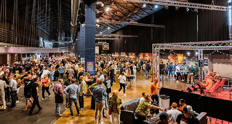 En stor lokal med högt i tak där många människor står och pratar och går runt och tittar på en utställning.