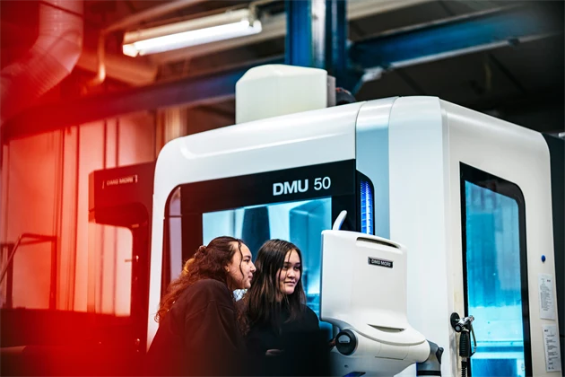 Två personer tittar på en skärm bredvid en stor maskin.