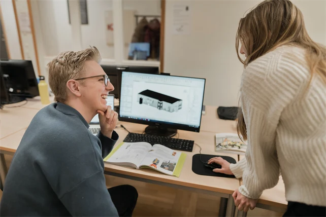 Två personer ser på varandra och ler framför en datorskärm.