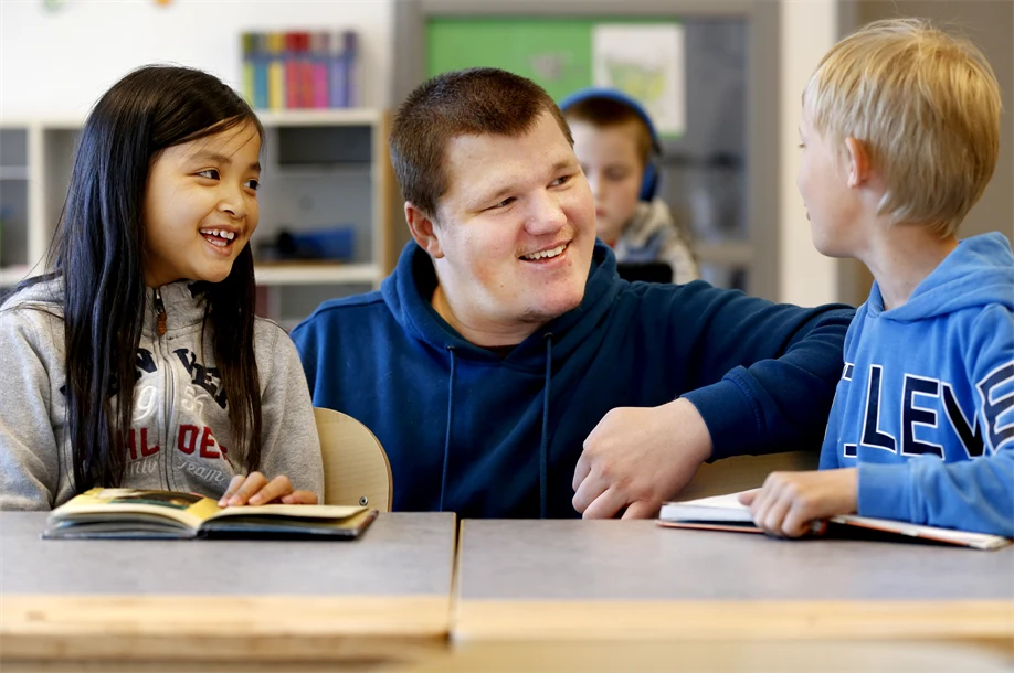 lärare pratar med två elever vid deras platser, de skrattar tillsammans