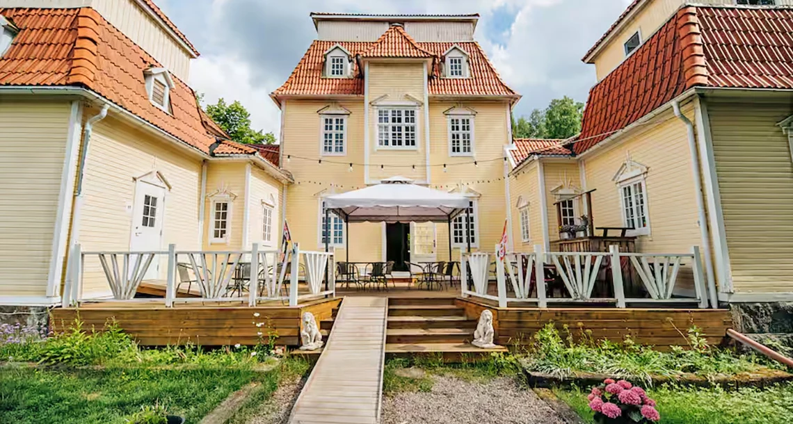 Ett stort trähus med paviljonger på båda sidor och en stor uteplats med bord och stolar