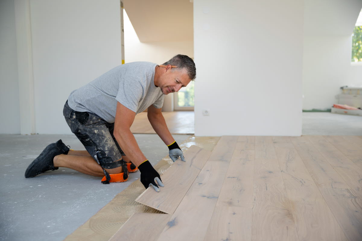 En golvläggare lägger ett trägolv i ett rum.