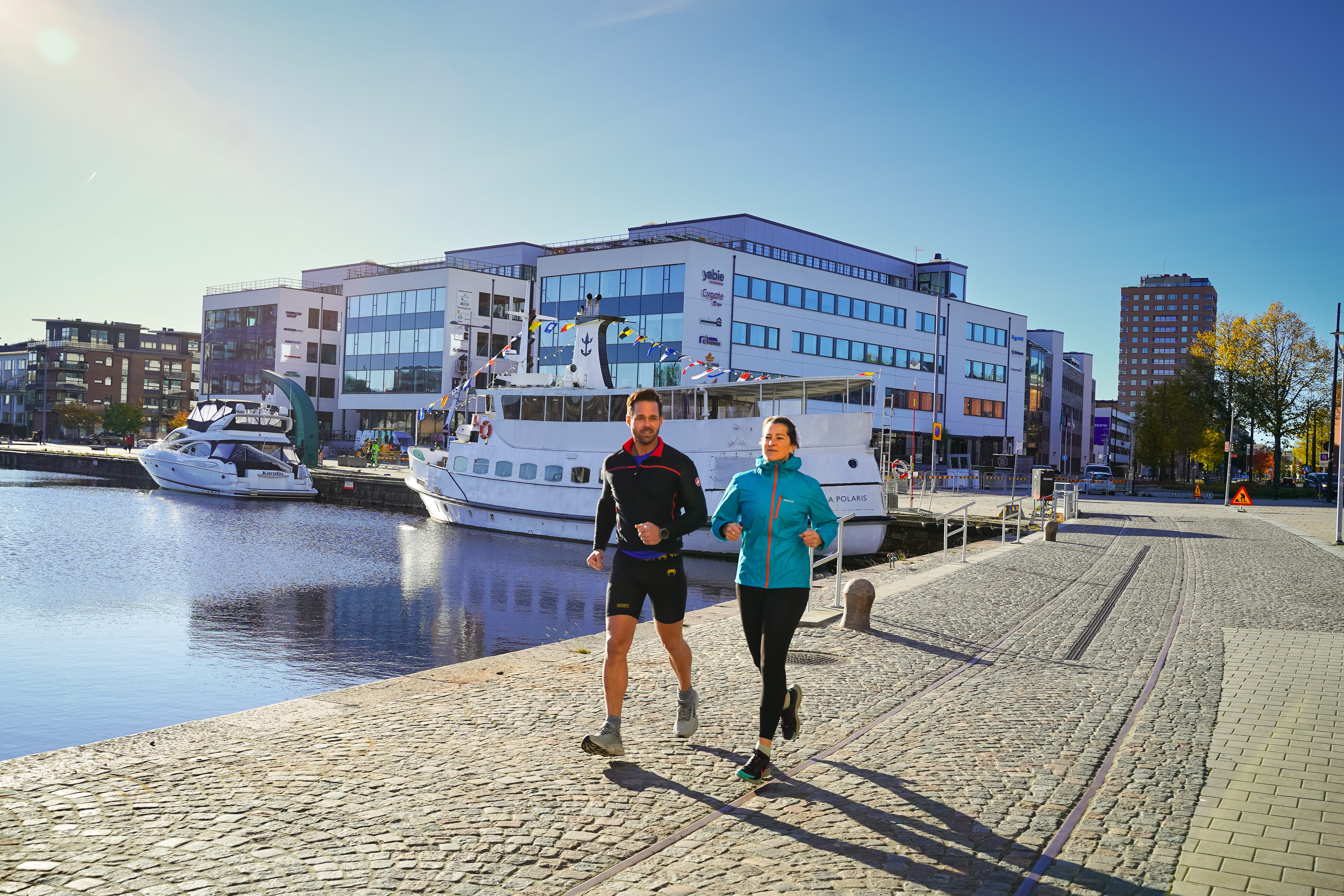 Två personer joggar längs vattnet vid Inre hamn. Båtar syns i bakgrunden