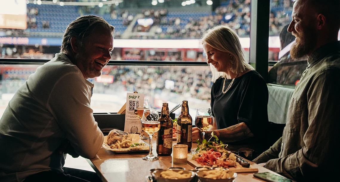 Två män och en kvinna sitter vid ett bord och äter och dricker gott.