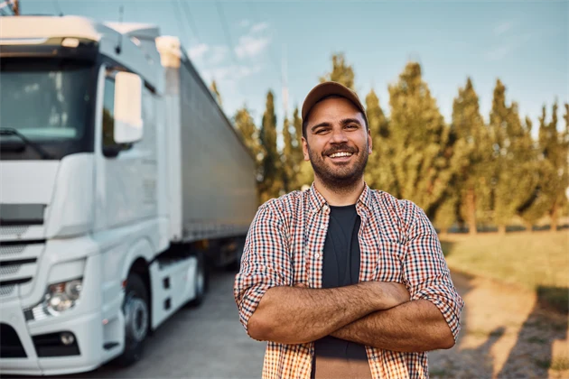 En person står bredvid en lastbil med armarna i kors och ler.