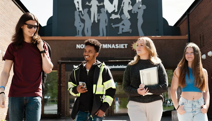 Fyra glada ungdomar går framför huvudentrén till Nobelgymnasiet.