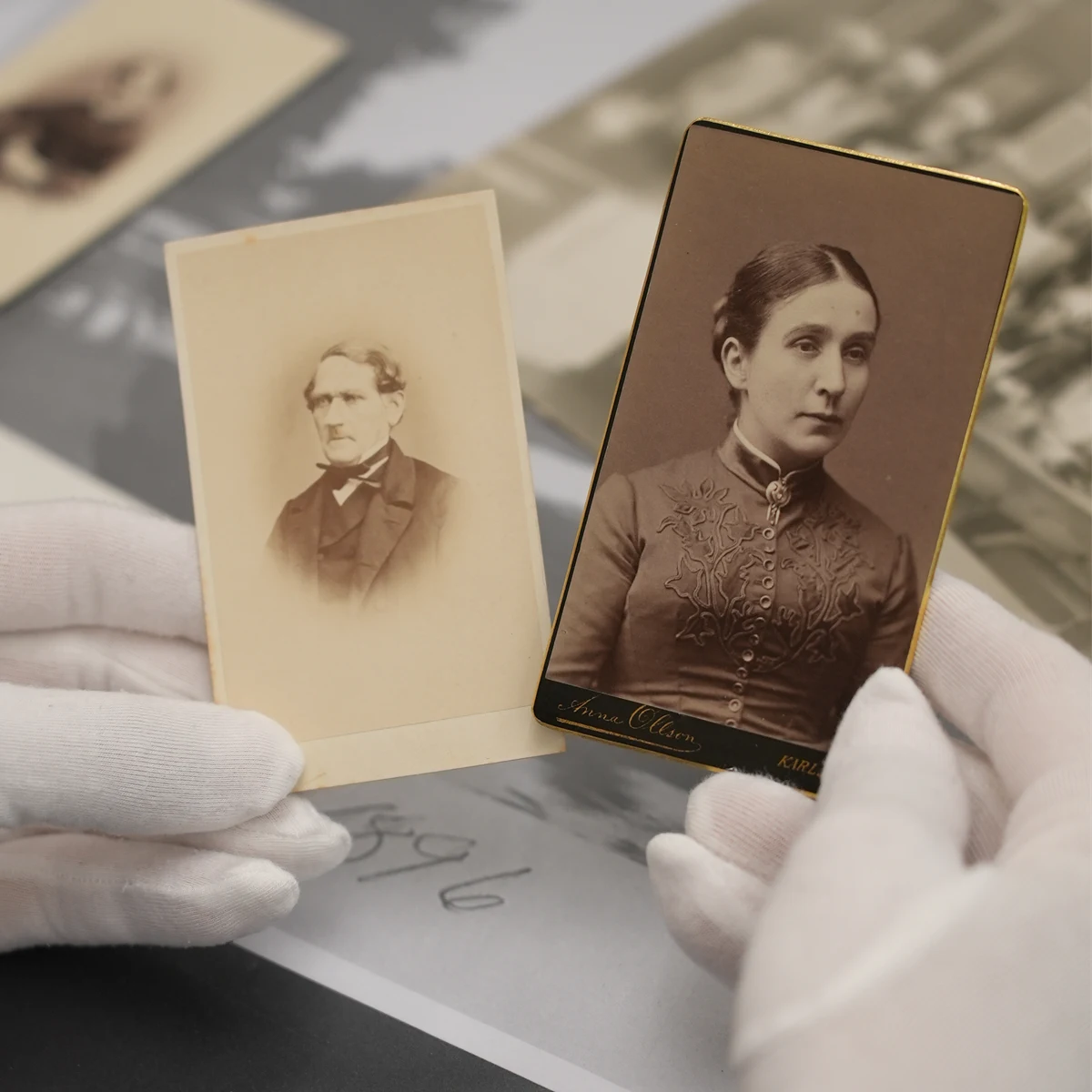 Händer klädda i bomullhandskar håller i gamla svartvita porträttfoton