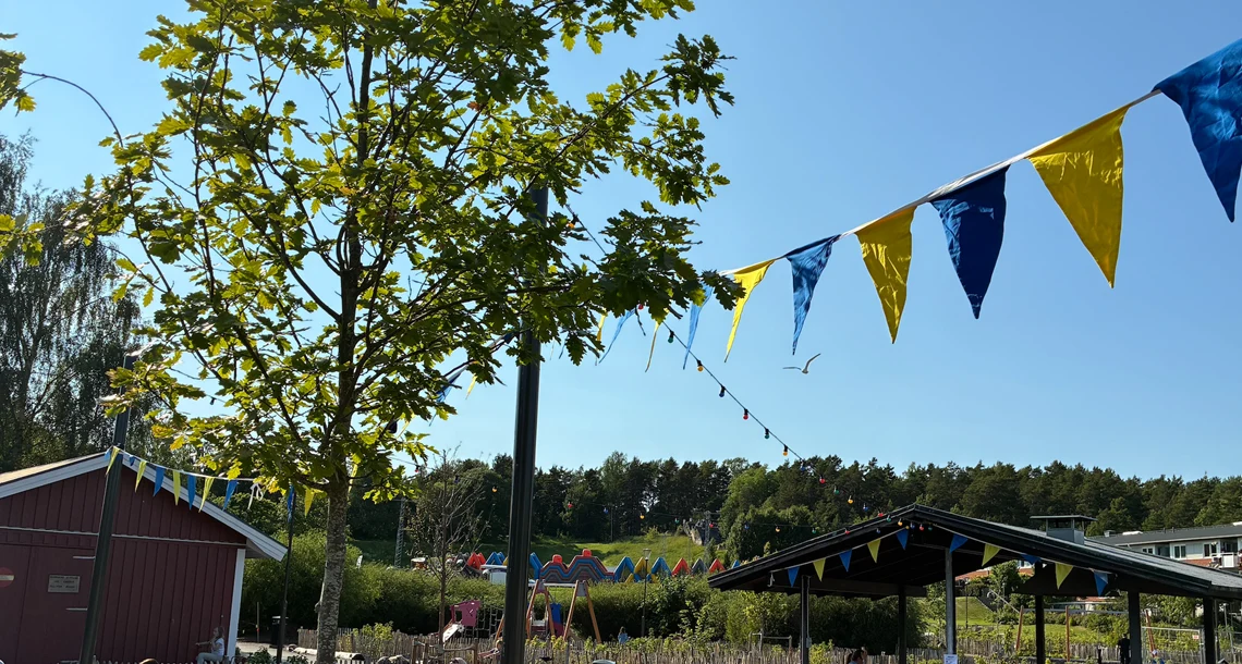 Parkleken Karmens utemiljö en solig sommardag, ett flaggspel med gula och blå vimplar hänger över marken