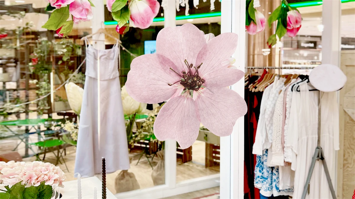 Bild tagen inne i en butik där det hänger kläder. Mitt i bilden en rosa blomma.