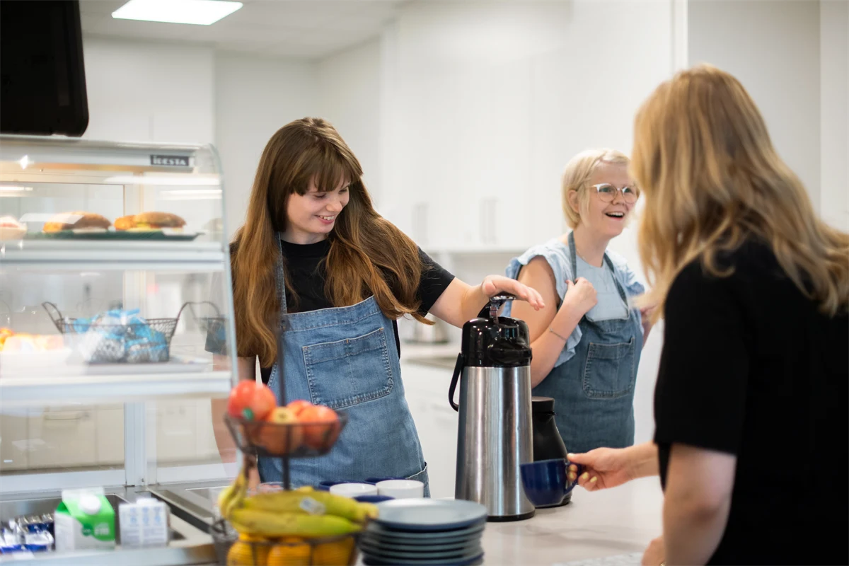 Två gymnasieelever jobbar i ett café och serverar kaffe bakom disk.
