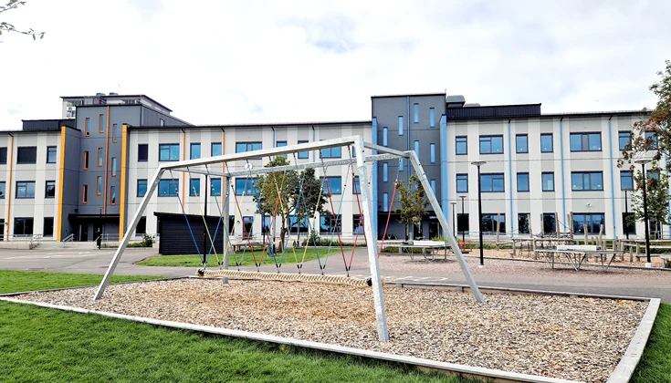 Skolgård med en stor kompisgunga man kan sitta fler barn på.