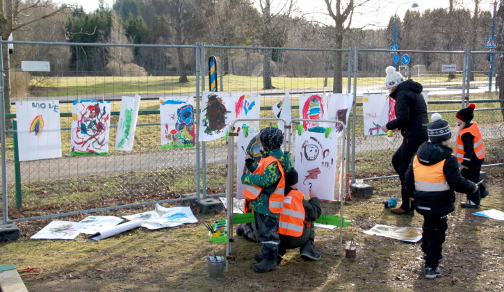 Barn målar teckningar utomhus och hänger upp på ett staket
