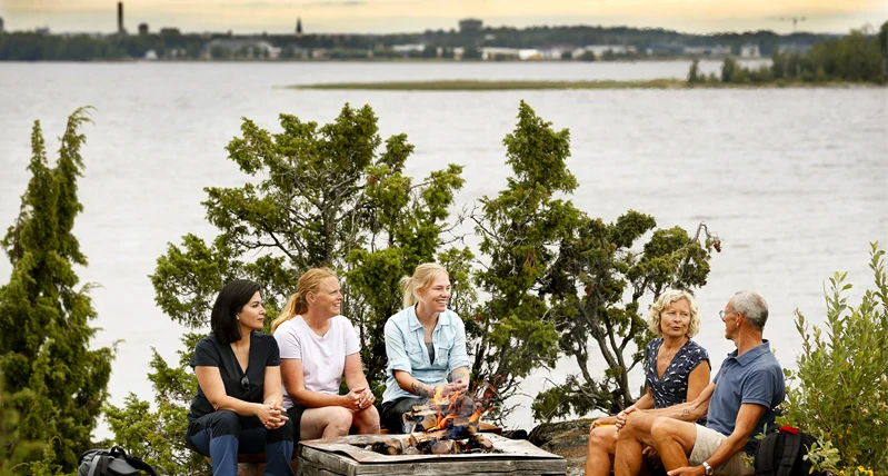 Fem personer sitter och grillar i skärgården.