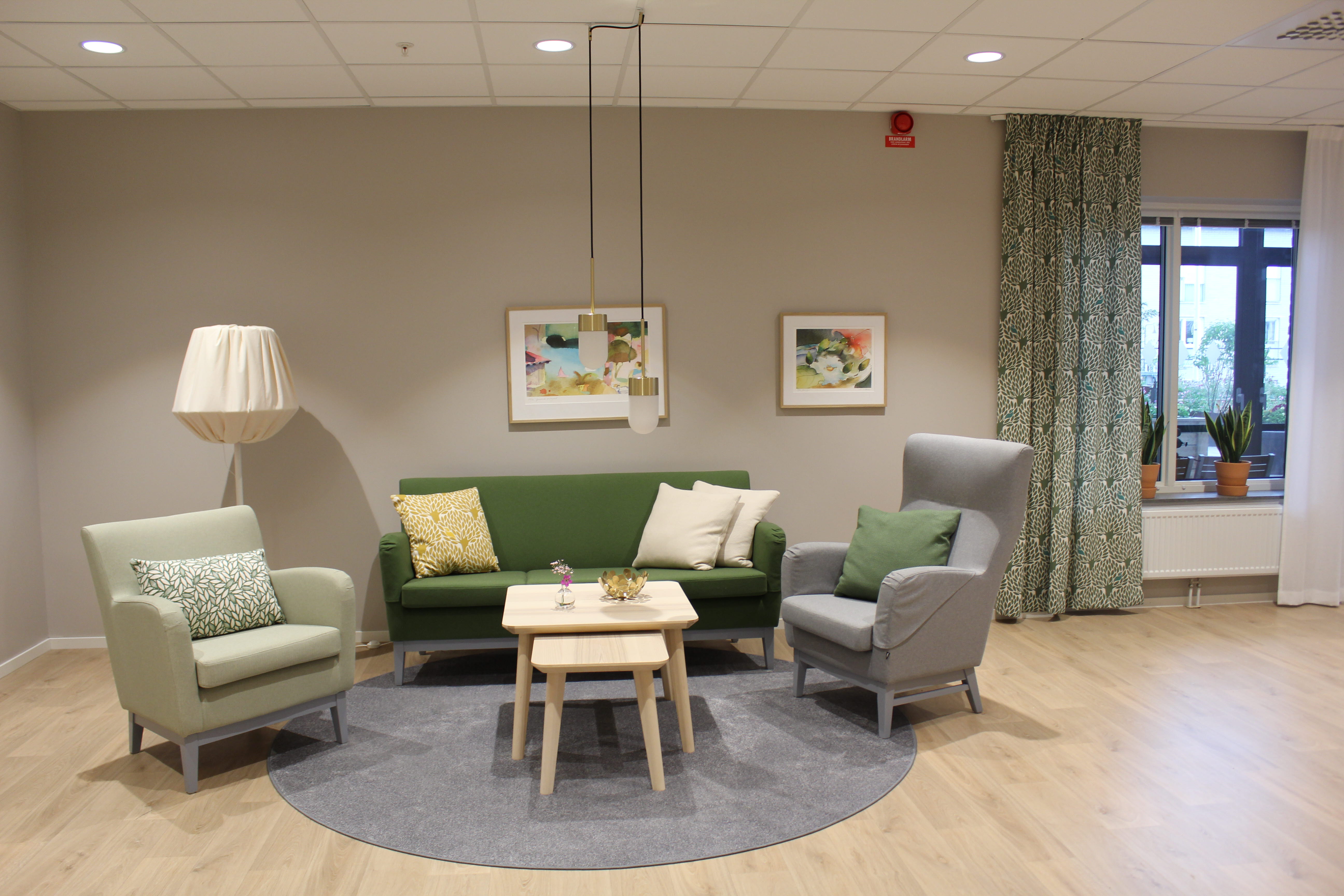 Del av en gemensamhetslokal med en grön soffa och två gröna och gråa fåtöljer med