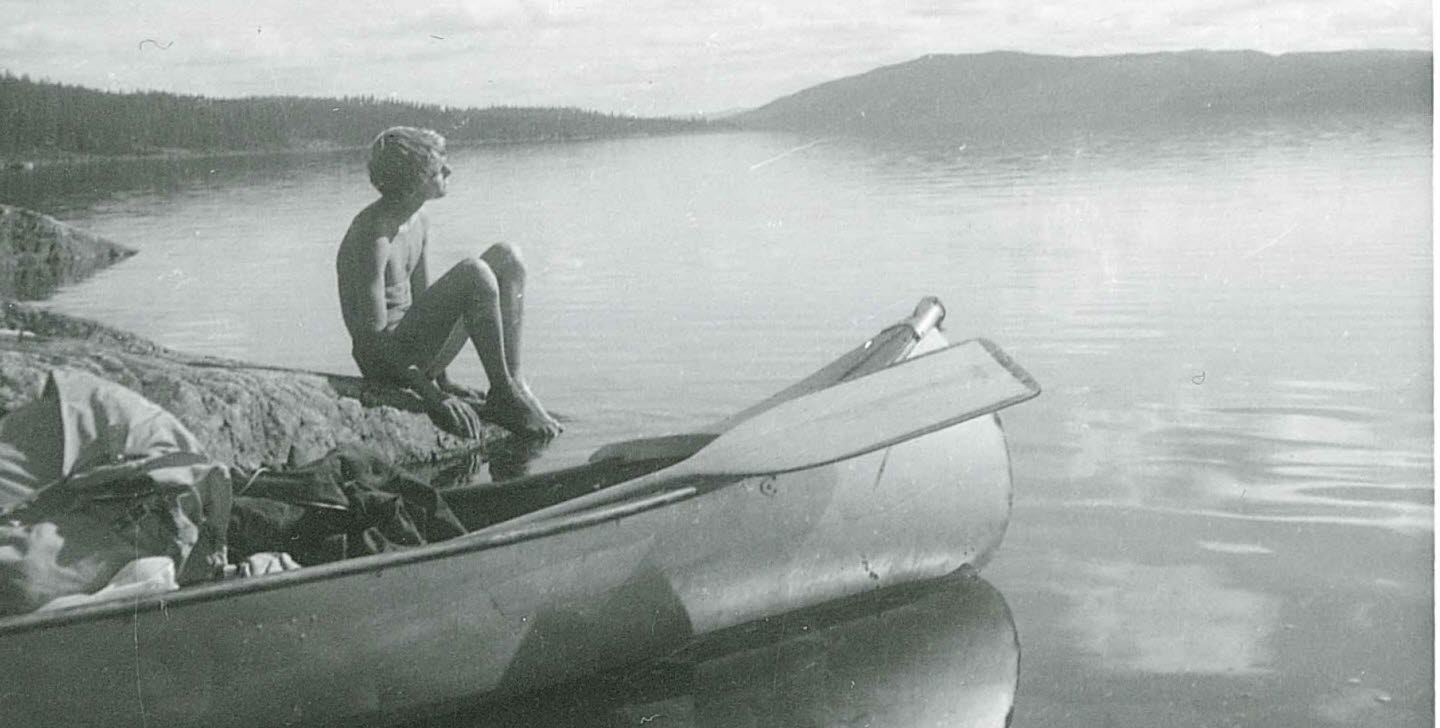Pojke sitter på klippa vid sjö med kanot framför sig