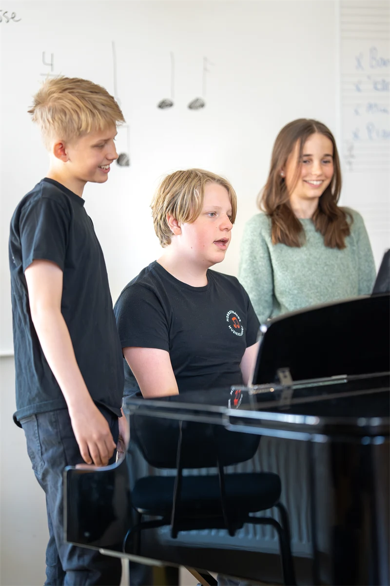 Grupp av elever som sjunger vid ett piano.