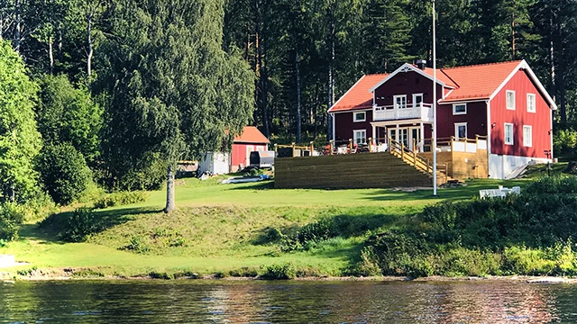 En stor röd villa framför en sluttande slänt ner mot vattnet