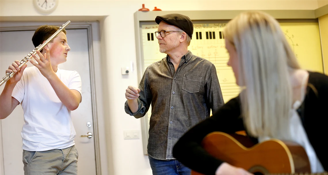 Två elever och en lärare som spelar gitarr i ett klassrum