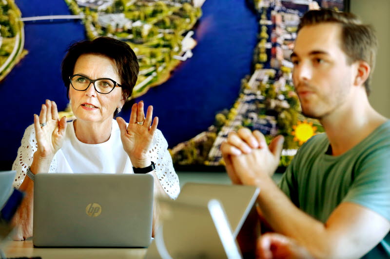 Kvinna och man sitter med laptops framför presentation i kontorsmiljö.