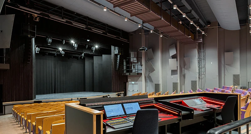 Ett mixerbord med reglage och skärmar och i  bakgrunden finns en stor scen