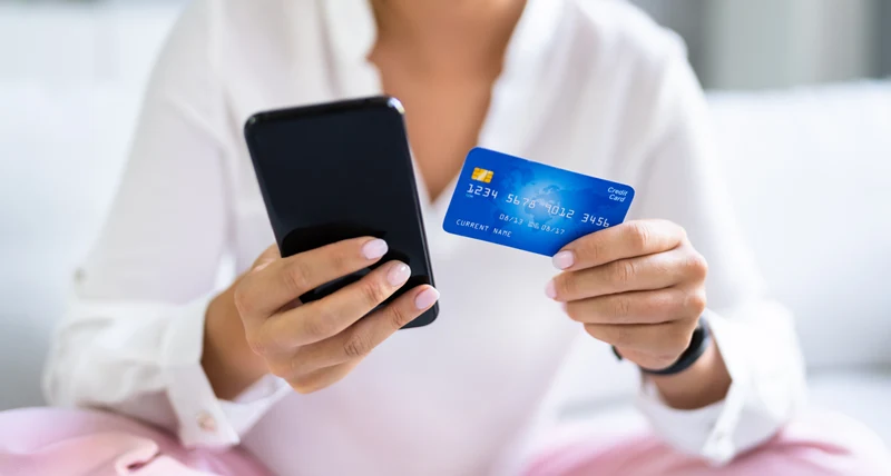 Människa som håller i en telefon och betalkort