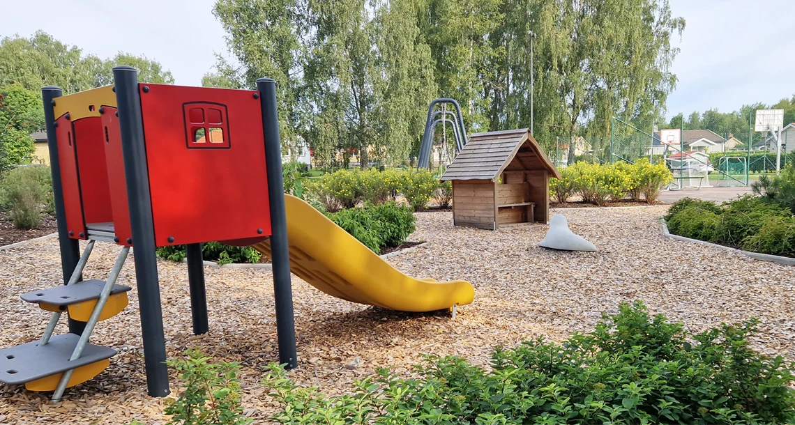 Bäcks lekplats i Vålberg med flisunderlag, gröna ytor, lekhus och rutchkana.