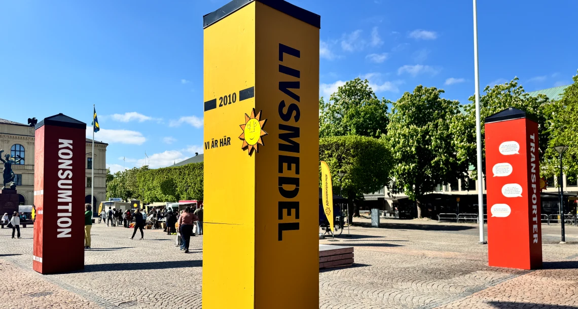 Bild på stolpar som står på ett torg. Himlen är klarblå