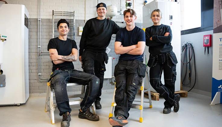 Tre killar och en tjej poserar för en gruppbild i en verkstadslokal.