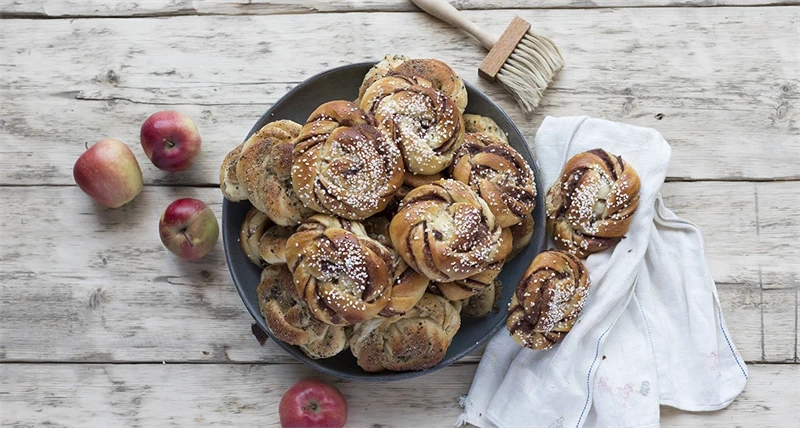 Ett fat med kanelbullar och röda äpplen bredvid på bordet