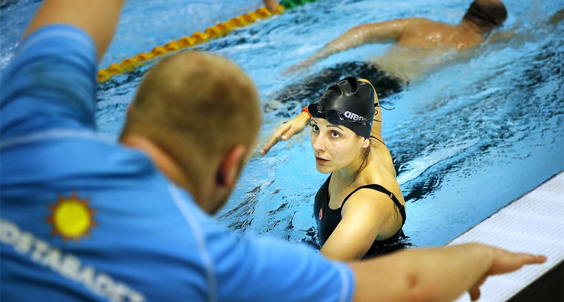 En siminstruktör visar crawlteknik för en kvinna i bassäng