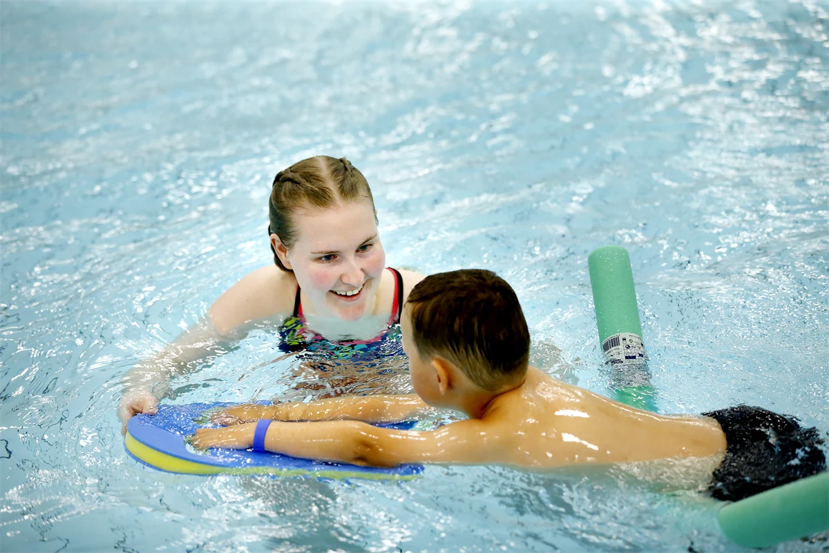 En person lär ett barn att simma i en inomhusbassäng.