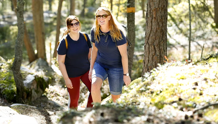 Två kvinnor vandrar bland klippblocken i I2-skogen.