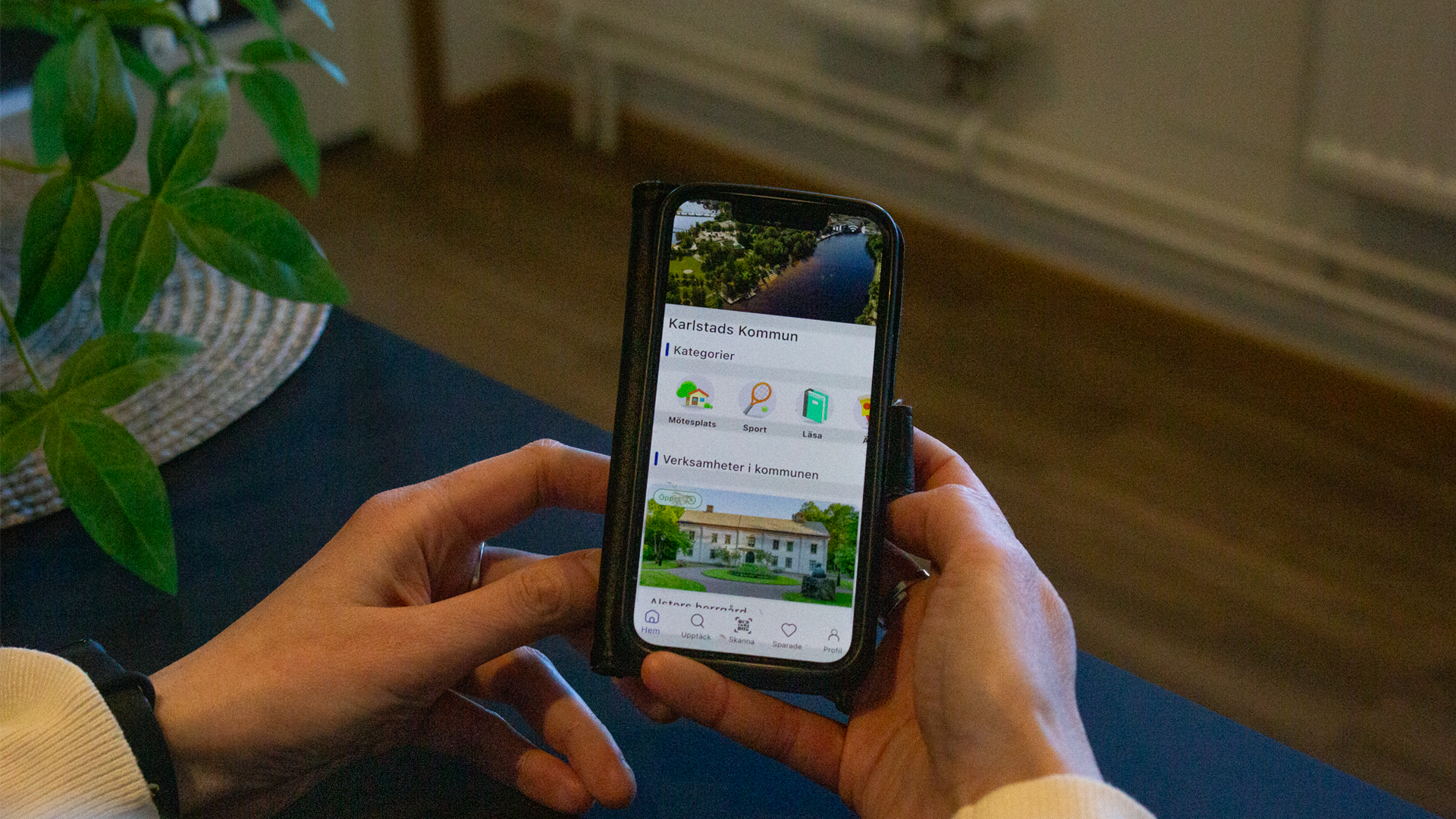 Två händer som håller i en mobiltelefon. På mobilen ser man appen öppna staden och det står "Karlstads kommun"