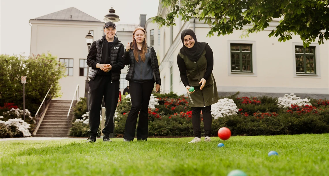 Tre elever spelar boule på en gräsmatta