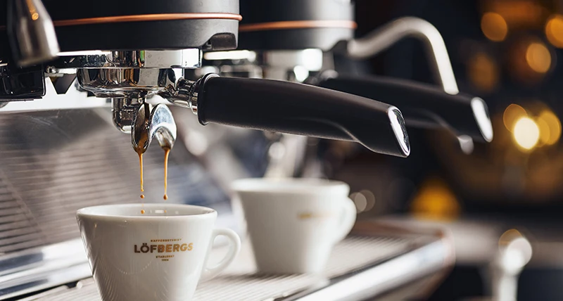 Två vita espressokoppar fylls på med kaffe i en kaffemaskin.